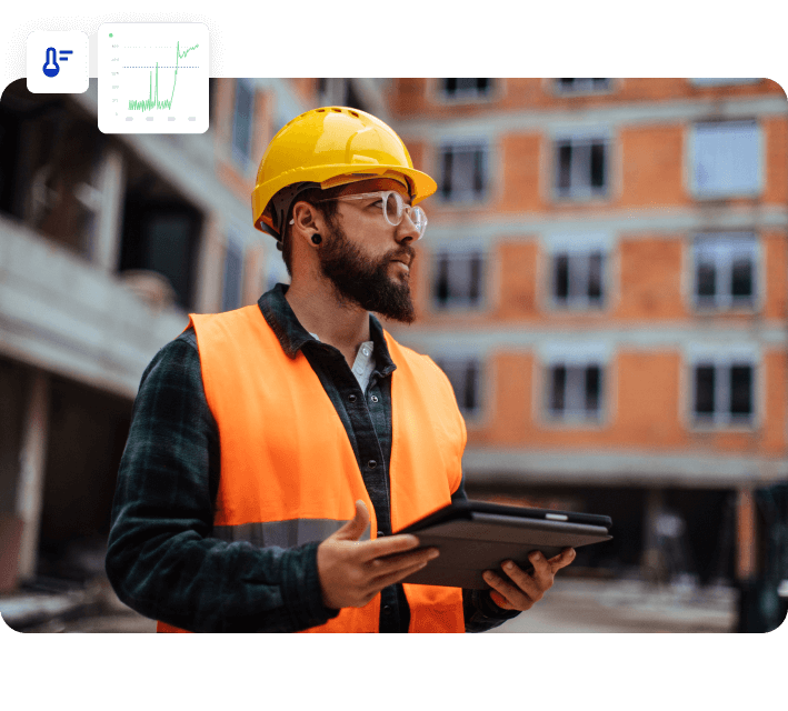 Man in orange safety vest and yellow hard hat holding a tablet at a building site with data overlay.