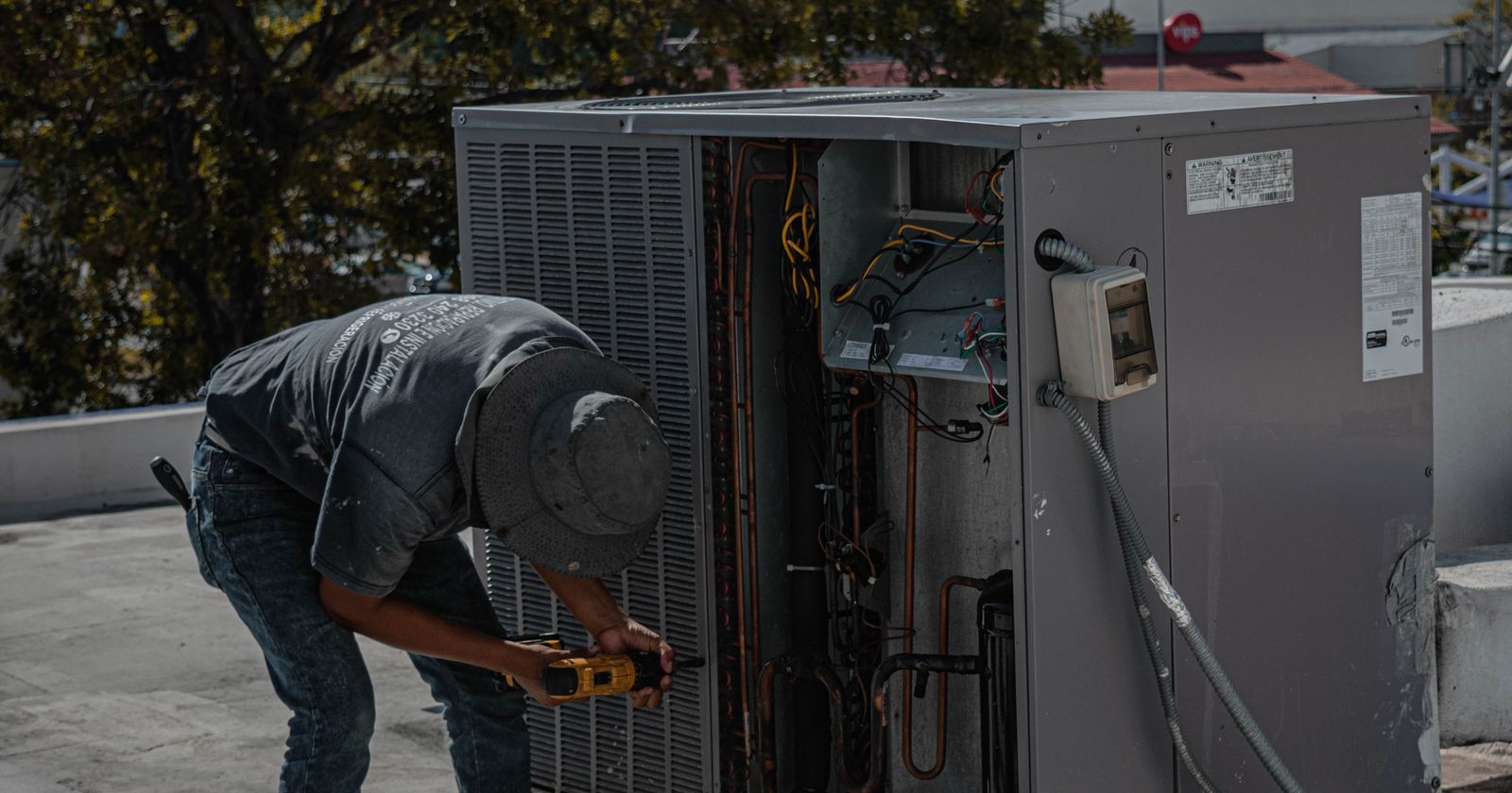 HVAC technician servicing an open commercial rooftop unit with a meter in hand
